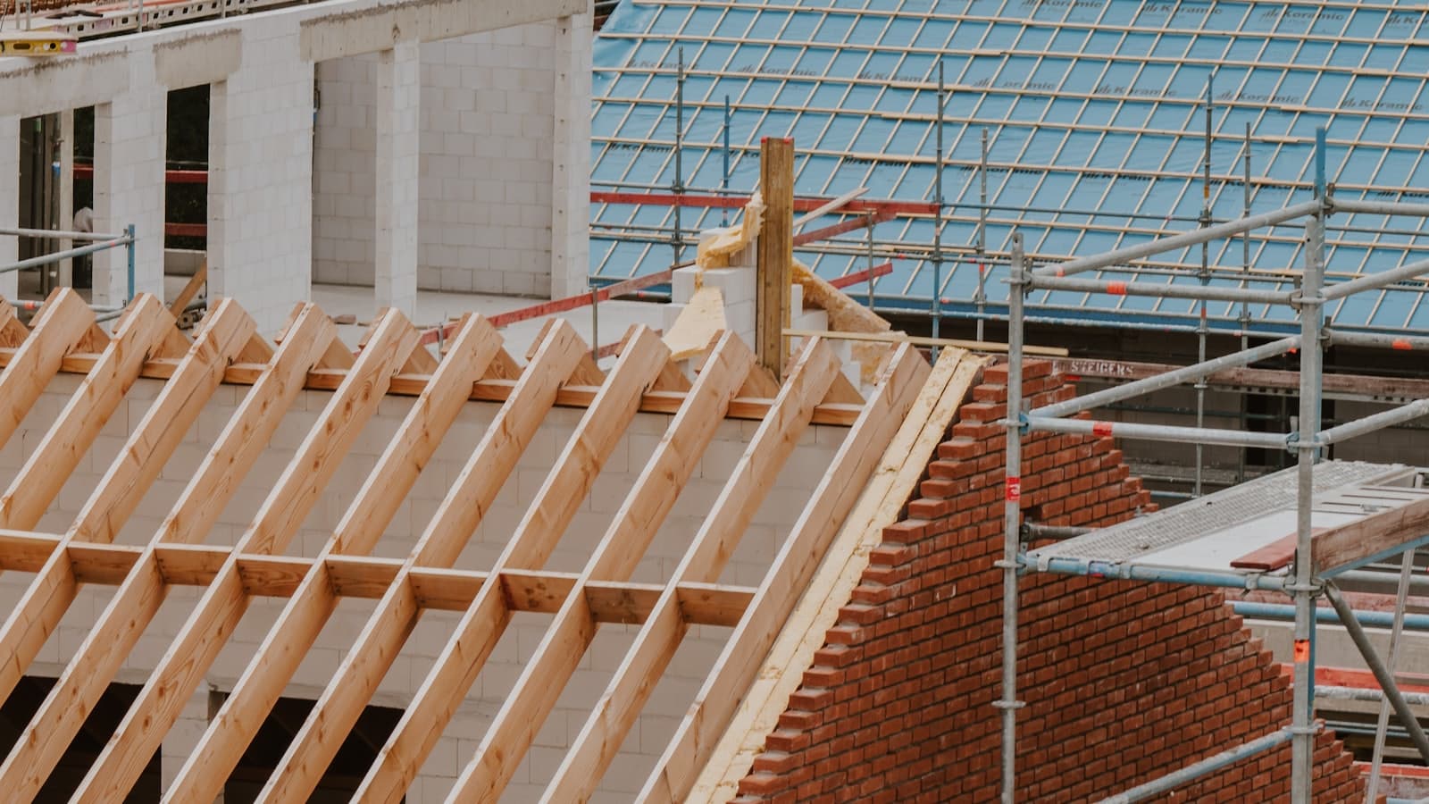 Houten dakspanten op een woning in aanbouw, met steigers langs een bakstenen topgevel
