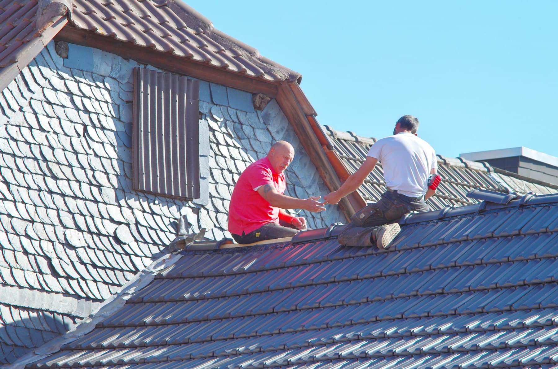 Twee dakdekkers aan het werk op een hellend dak met leien