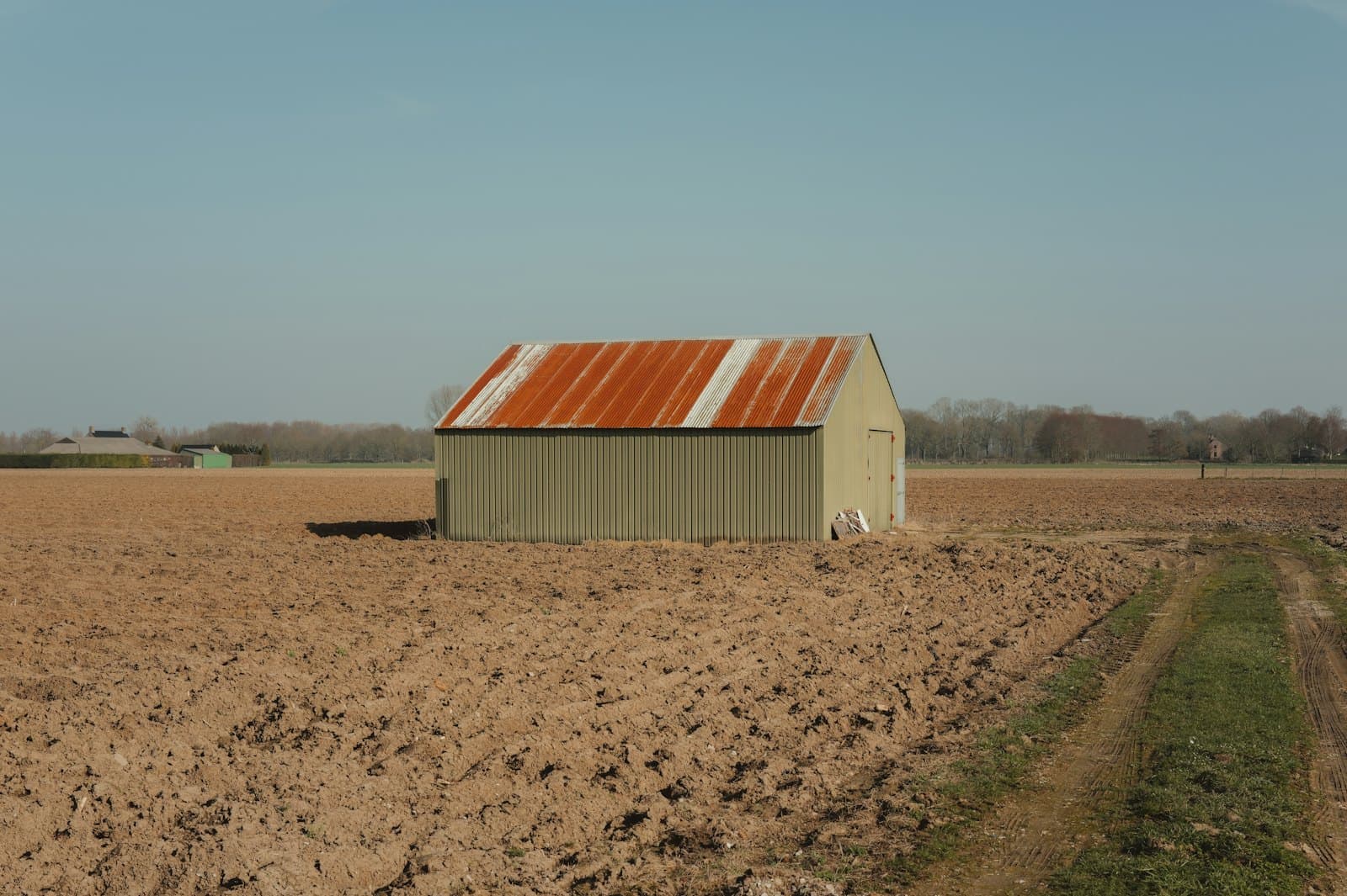 Kleine schuur met een golfplaten dak midden in een Nederlands akkerlandschap onder een heldere lucht