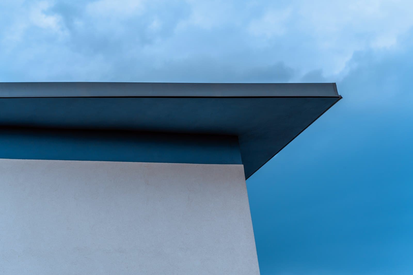 Dakrand van een plat dak met een strakke aluminium daktrim tegen een bewolkte lucht
