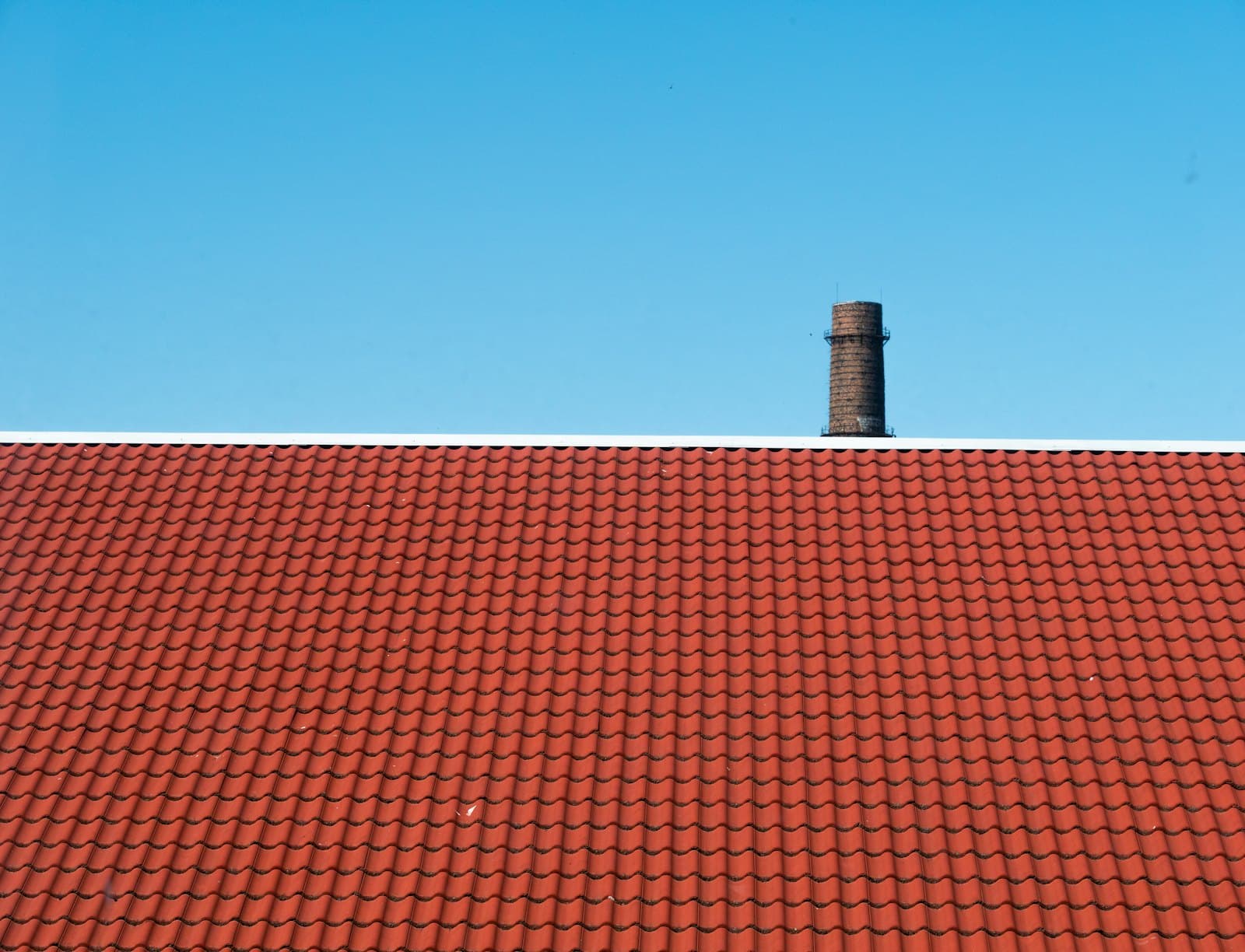 Rood pannendak met schoorsteen tegen een strakblauwe lucht