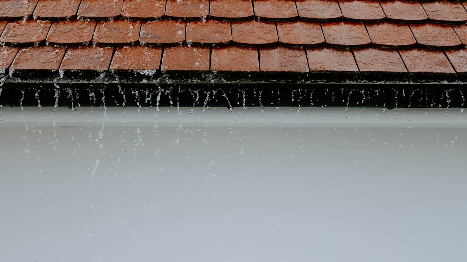 Regenwater stroomt over de dakrand en de goot van een pannendak tijdens een flinke bui