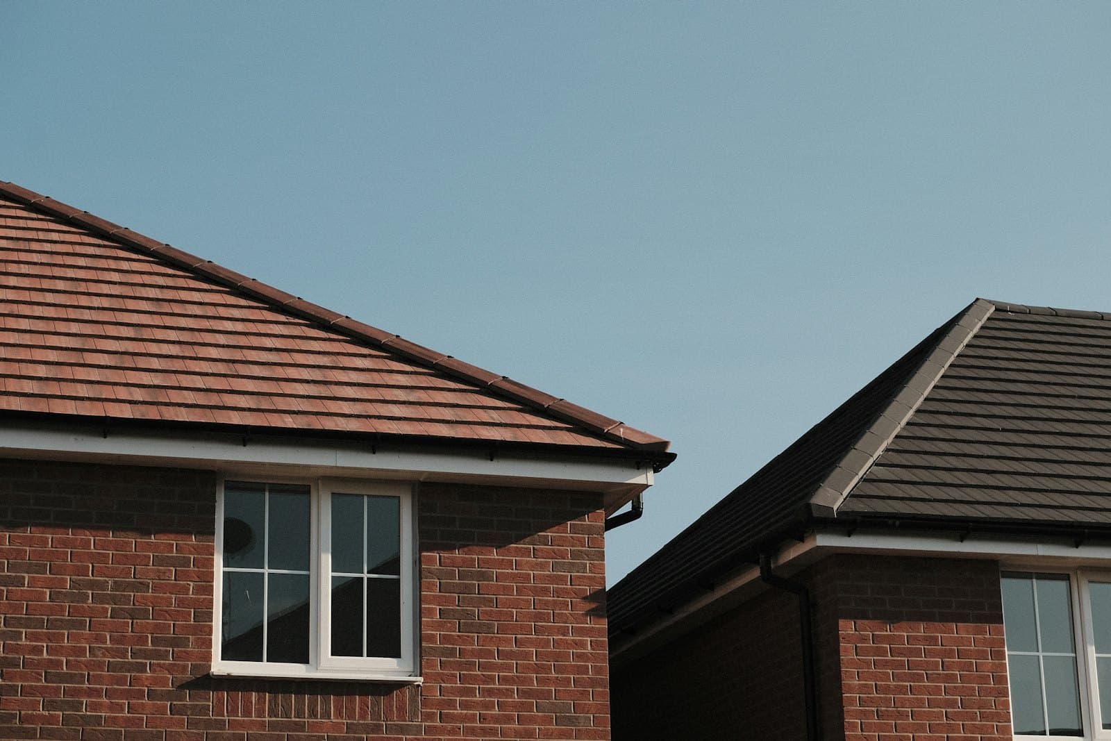 Twee woningen met een pannendak waarbij de nokvorsten en de hoekkepers duidelijk zichtbaar zijn tegen een heldere lucht