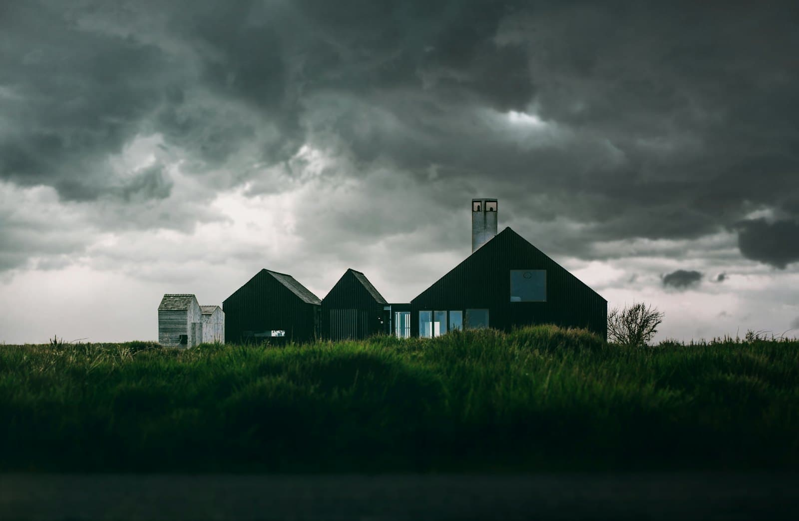 Woningen met een steil pannendak en een schoorsteen onder een zware, donkere stormlucht