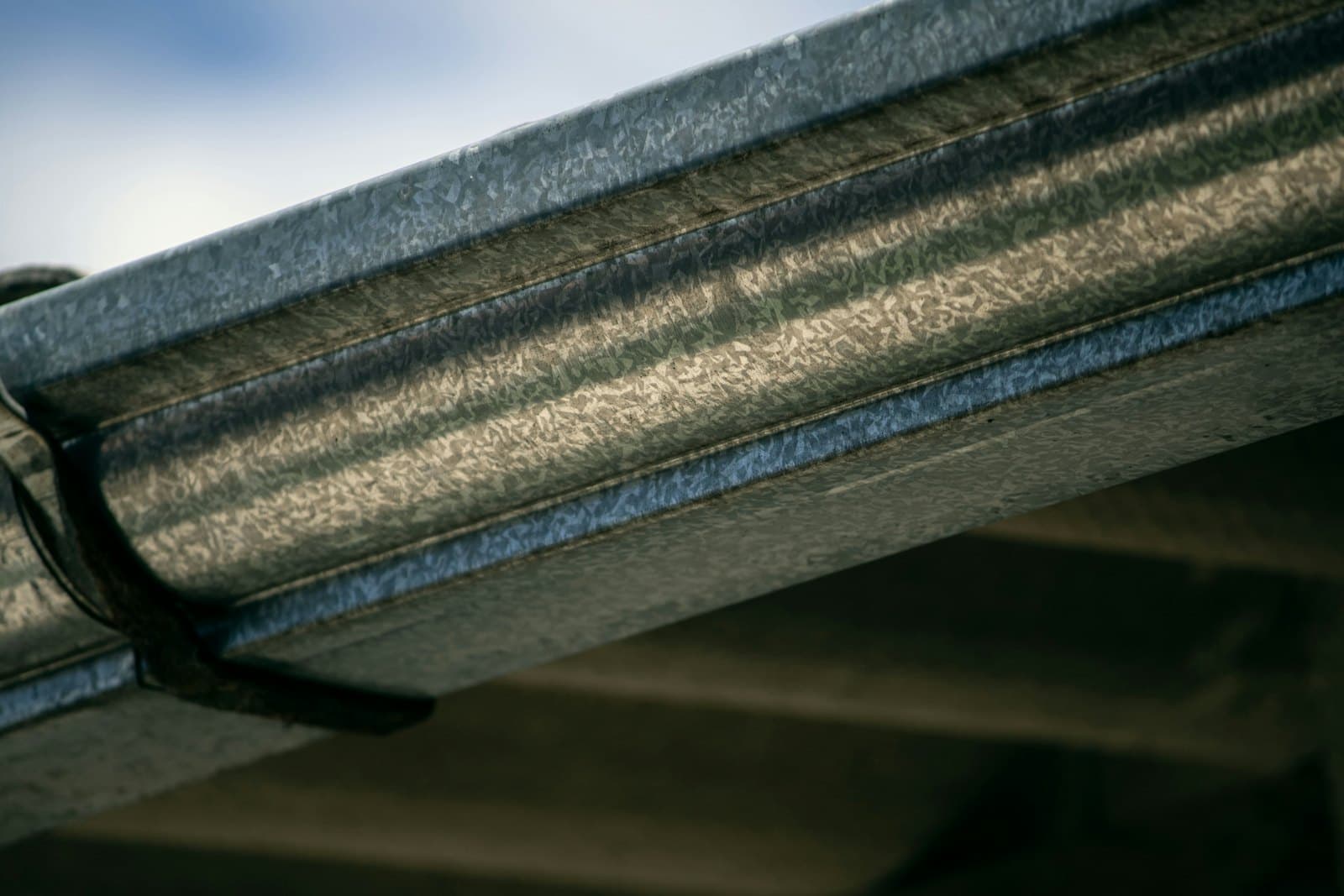Close-up van een zinken dakgoot met zichtbare gootbeugel langs de dakrand van een woning